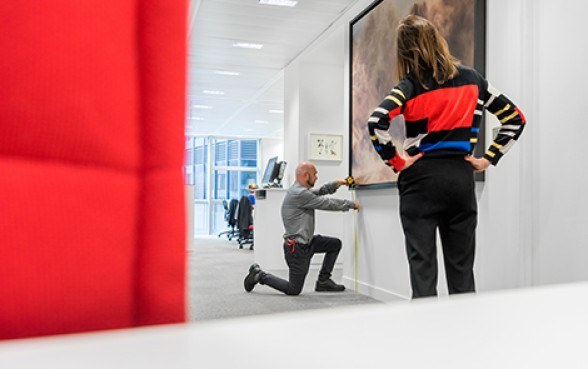 Zwei Menschen richten ein Gemälde an einer Wand aus